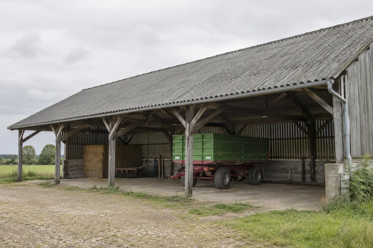 Hangar agricole ouvert abritant une remorque sous une ancienne couverture grise
