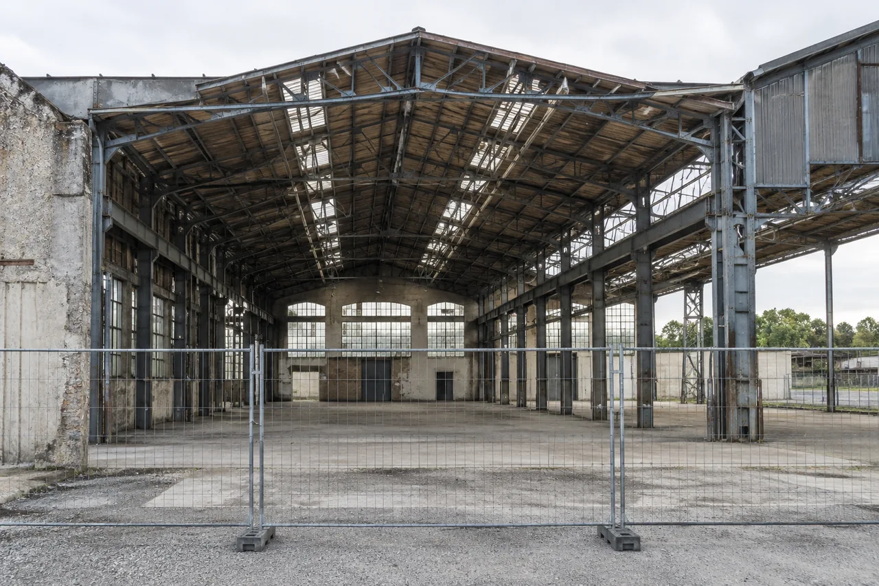 Halle industrielle vide à charpente métallique derrière une clôture fermée